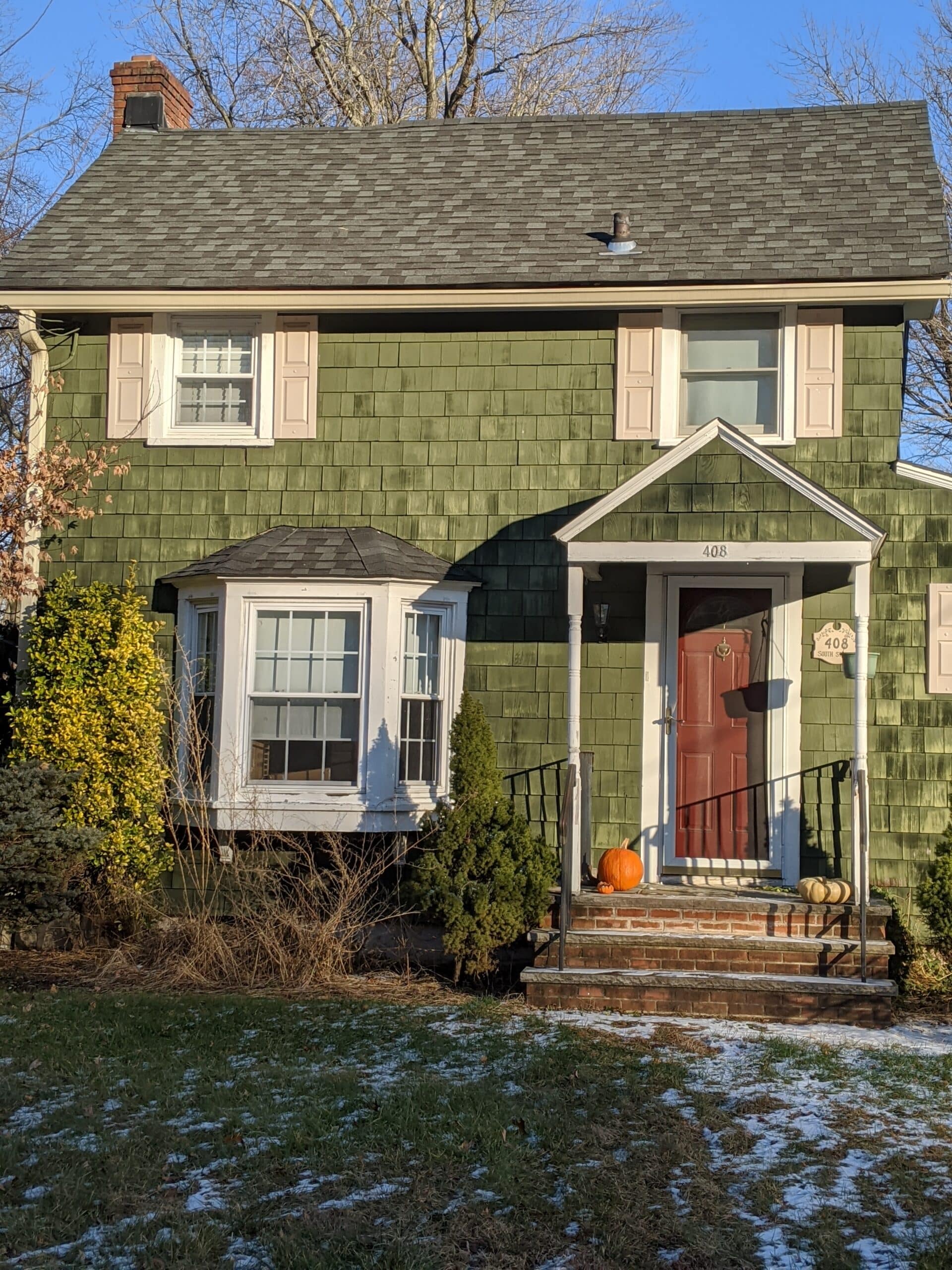 A older green home with a pumpkin on its stoop
