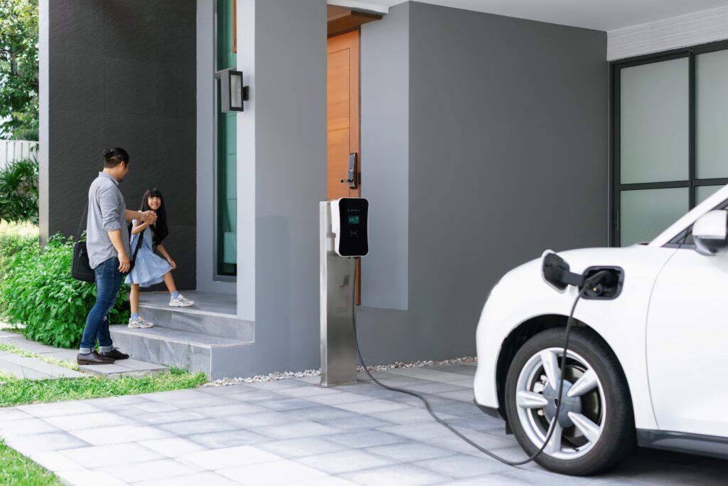 a father and daughter entering a home next to the garage where their electric vehicle is charging