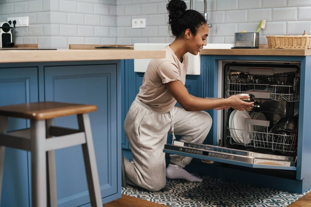 A woman smiling while using dishwasher at home kitchen - how to be energy efficient at home