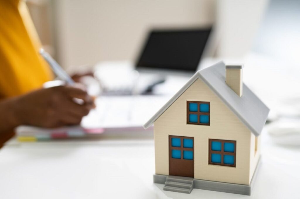 a person making note in a binder behind a small home on a desk