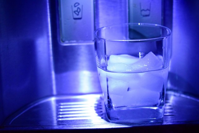 a small glass of ice sits in the curve of a refrigerator ice dispenser