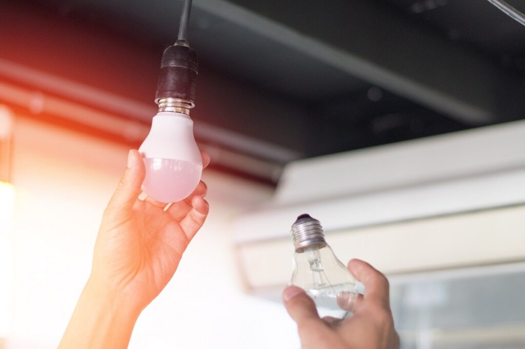 a homeowner switching out a normal light bulb for an LED one - how to be energy efficient at home