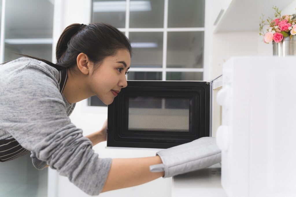a woman using a mitt to take food out of a microwave - how to be energy efficient at home