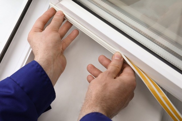 a homeowner applying weather stripping to a window