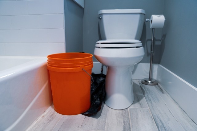 a bucket and garbage bag next to a toilet