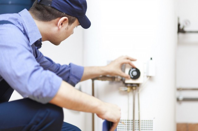 a home professional in a hat turning down the heat on a hot water heater