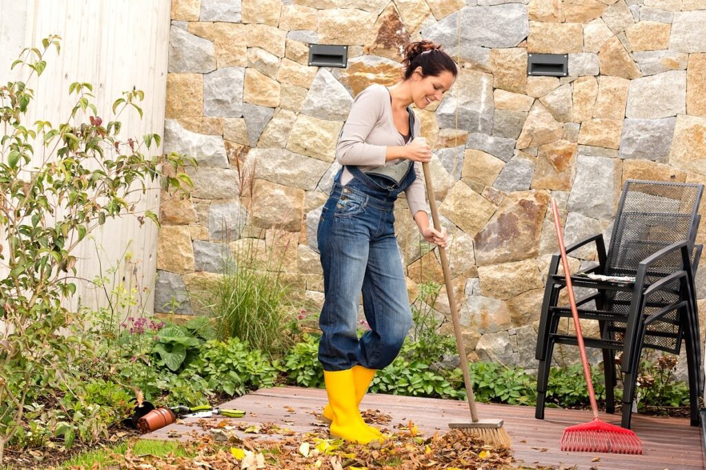 a woman sweeping leaf litter from her porch - keep ticks out of your yard