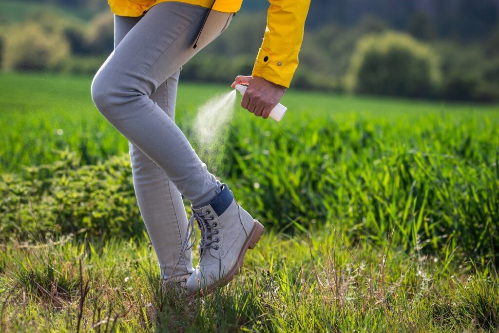 Woman hiker spraying insect repellent against tick on her legs and boots