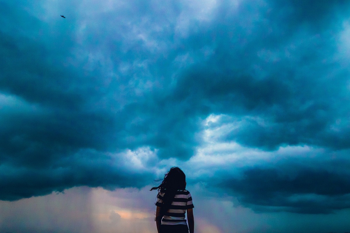a woman standing underneath storm clouds - hurricane preparedness tips