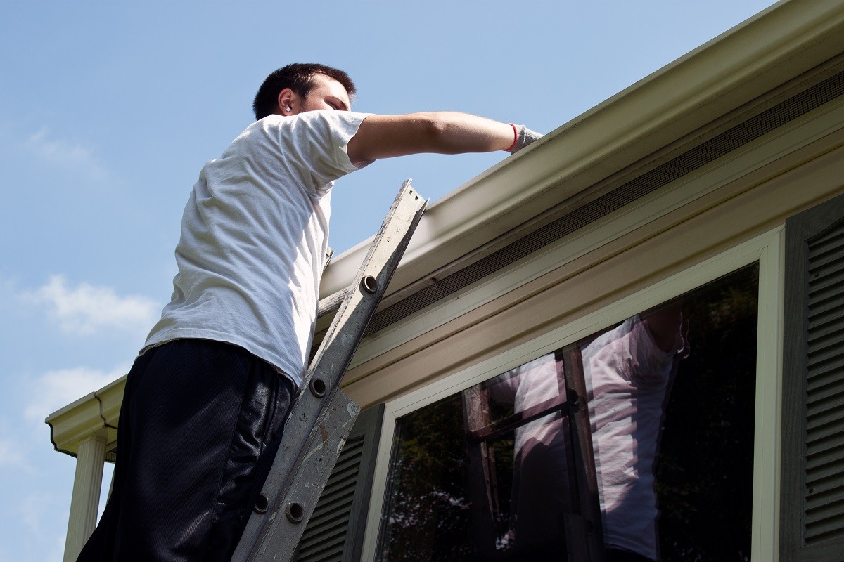 a homeowner cleaning out the gutters - fall home maintenance