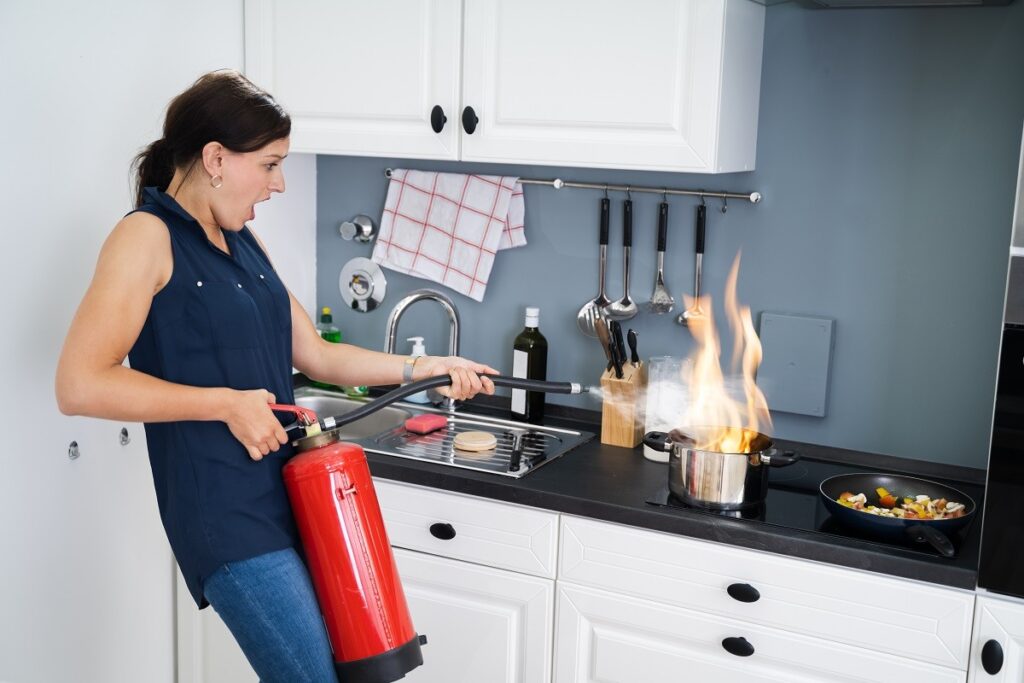 woman using a fire extinguisher on a small kitchen fire