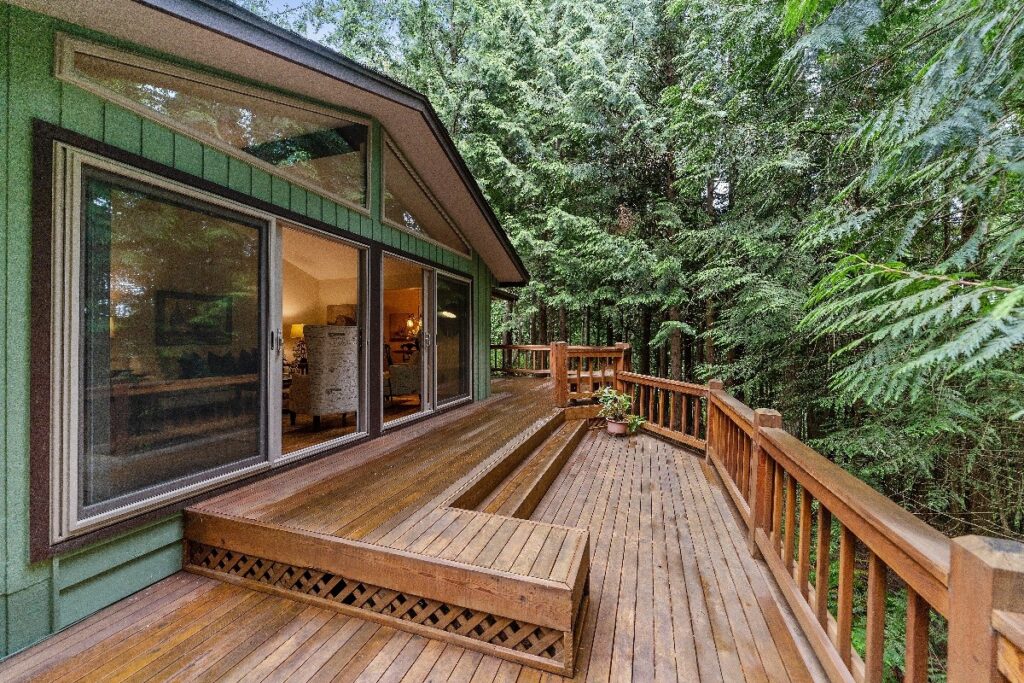 wooden deck attached to a green house in the woods