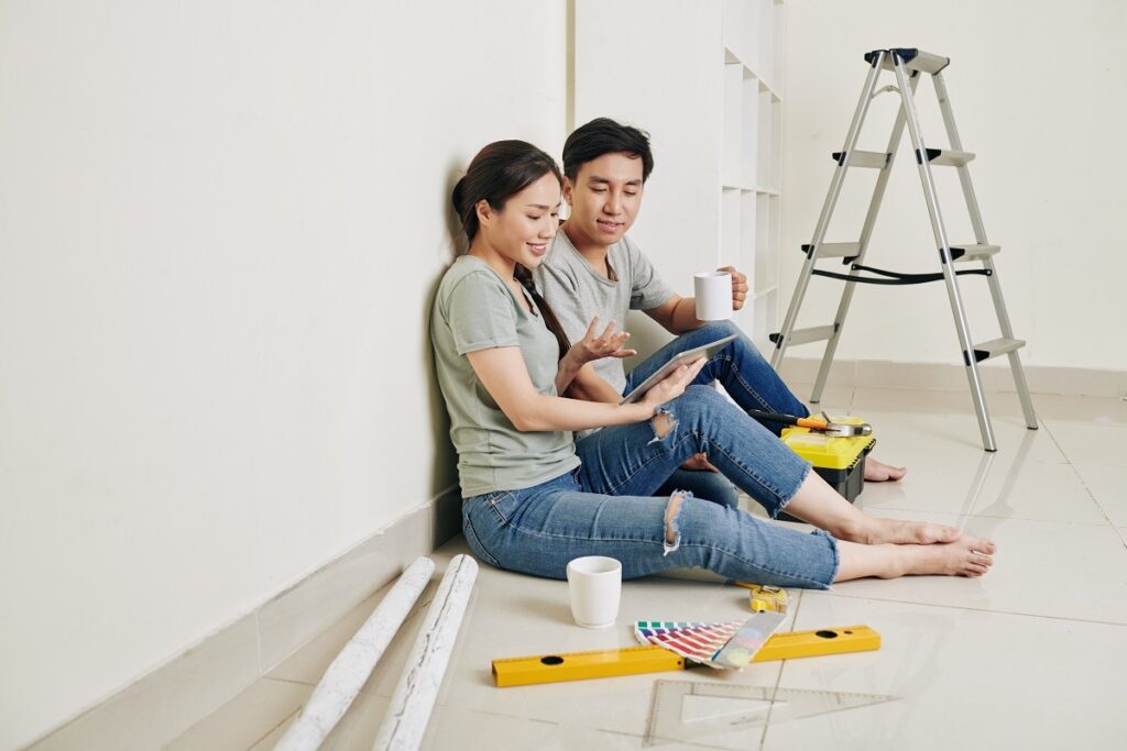 A couple sitting against a wall, taking a break from painting