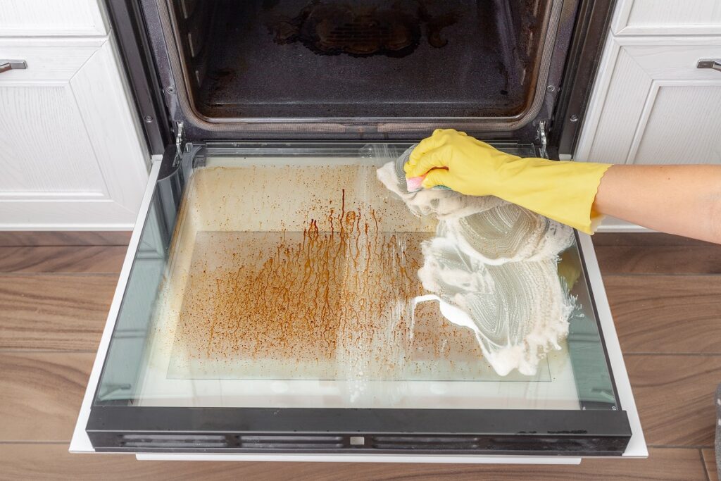 A person wearing a glove and cleaning the oil off the oven door