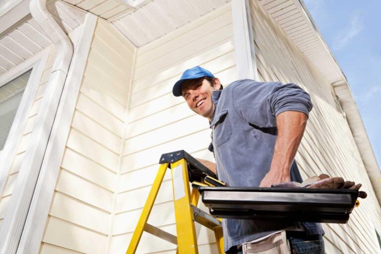 a handyman with a toolbox smiling by a downspout
